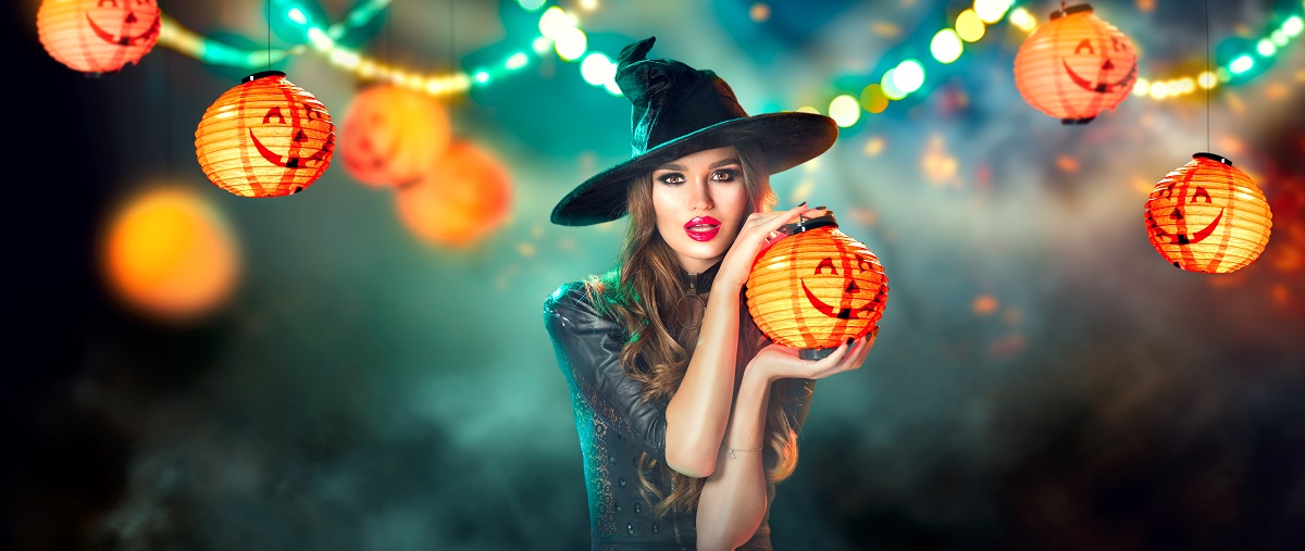 O femeie frumoasă care ține în mână un dovleac și pozează într-unul din principalele costume de Halloween făcute acasă