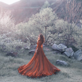 Fată frumoasă îmbrăcată într-o rochie lungă roșie stă într-o pădure