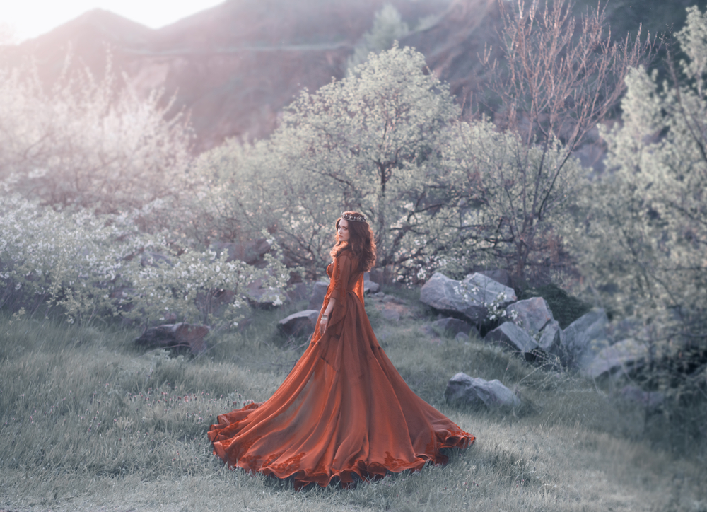Fată frumoasă îmbrăcată într-o rochie lungă roșie stă într-o pădure
