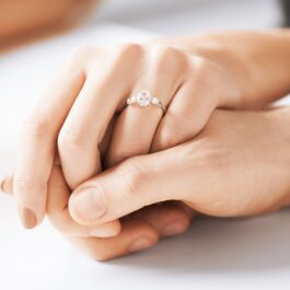 Două mâini, una de femei și una de bărbat, care se țin una pe cealaltă pentru a ilustra piatra prețioasă folosită pentru realizarea inelului de logodnă