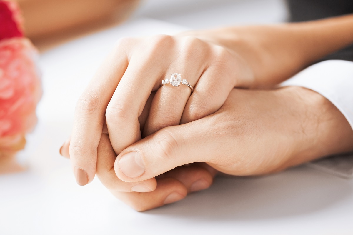 Două mâini, una de femei și una de bărbat, care se țin una pe cealaltă pentru a ilustra piatra prețioasă folosită pentru realizarea inelului de logodnă