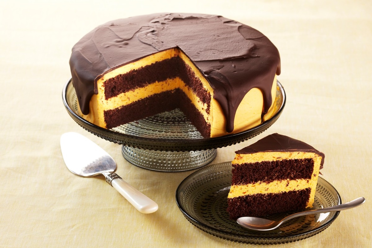 Tort cu cremă de dovleac copt și glazură de ciocolată porționat pe platou și pe farfurie, alături de o spatulă de tort
