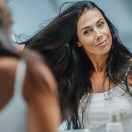 O femeie frumoasă cu părul lung care se uită în oglindă având una din principalele tunsori recomandate pentru femei după vârsta de 40 de ani