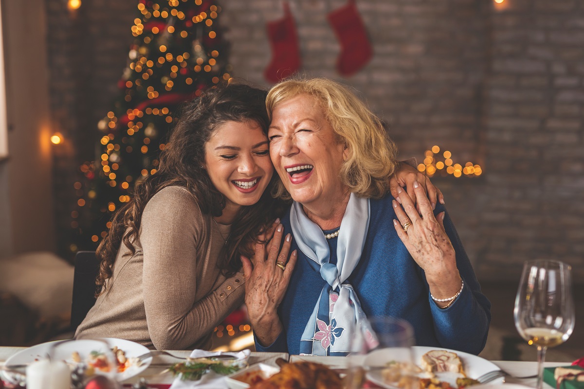 O fiică și o mamă care se îmbrățișează în fața unei mese festive de Crăciun pentru a ilustra modul în care CaTine.ro onorează mamele de Crăciun