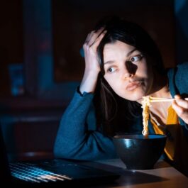 O femeie tânără care mănâncă noaptea în timp ce lucrează la laptop