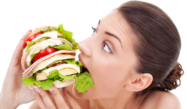 O femeie care încearcă să mănânce un sandviș imens