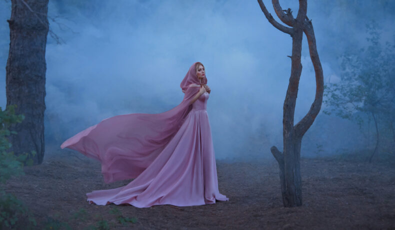Fată frumoasă îmbrăcată într-o rochie roz, lungă stă într-o pădure întunecată