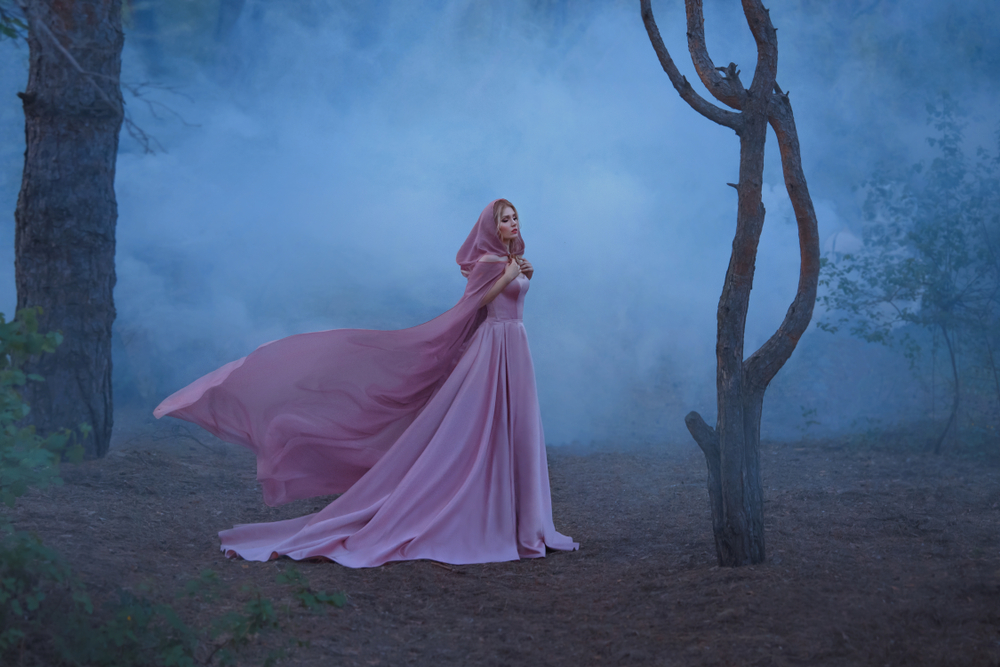 Fată frumoasă îmbrăcată într-o rochie roz, lungă stă într-o pădure întunecată