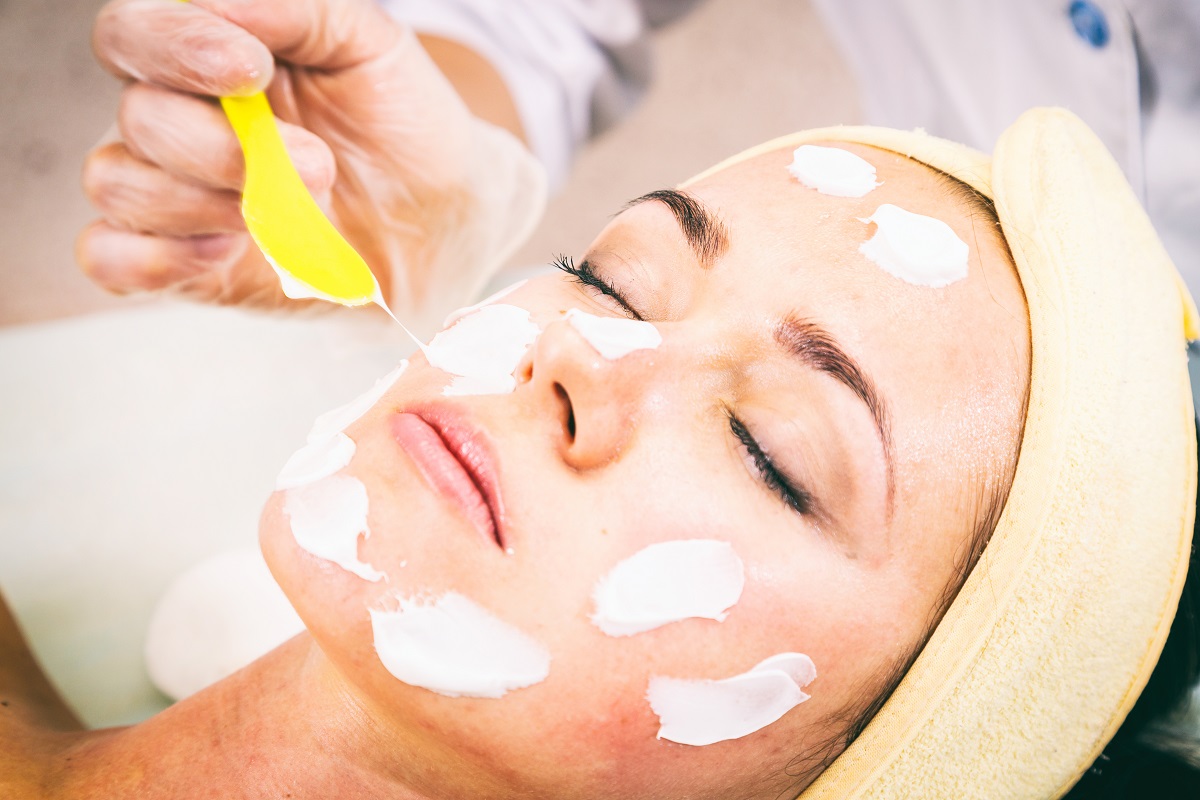 O femeie frumoasăc are stă cu o cremă albă pe față la o procedură cosmetică pentru a ilustra de ce apar punctele de grăsime pe față