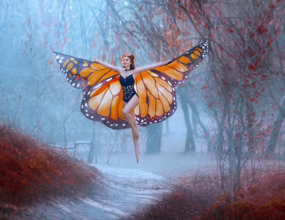 Fată frumoasă îmbrăcată în aripi de fluture stă în pădure