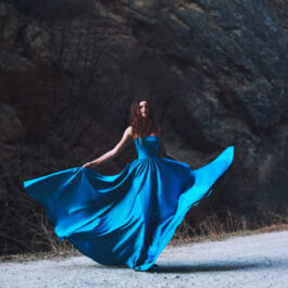 Fată frumoasă îmbrăcată într-o rochie albastră stă în pădure