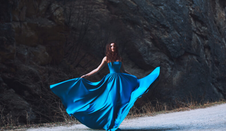Fată frumoasă îmbrăcată într-o rochie albastră stă în pădure