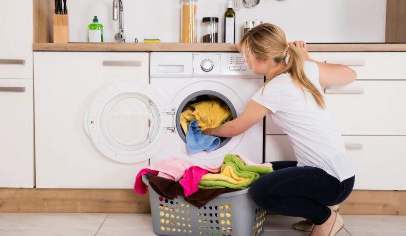 O femeie care bagă rufe la mașina de spălat rufe