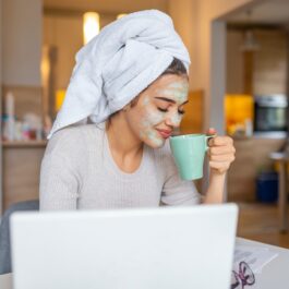 O femeie frumoasă cu mască și prosop pe cap care bea o cafea pentru a ilustra unul din obiceiurile care te pot face să fii productivă dimineața