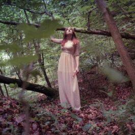 Fată frumoasă îmbrăcată într-o rochie lungă, roz în pădure