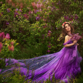 Fată frumoasă îmbrăcată într-o rochie mov, lungă, stă în pădure