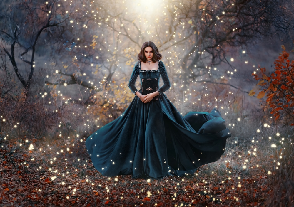 Fată frumoasă îmbrăcată într-o rochie lungă stă într-o pădure înconjurată de lumini