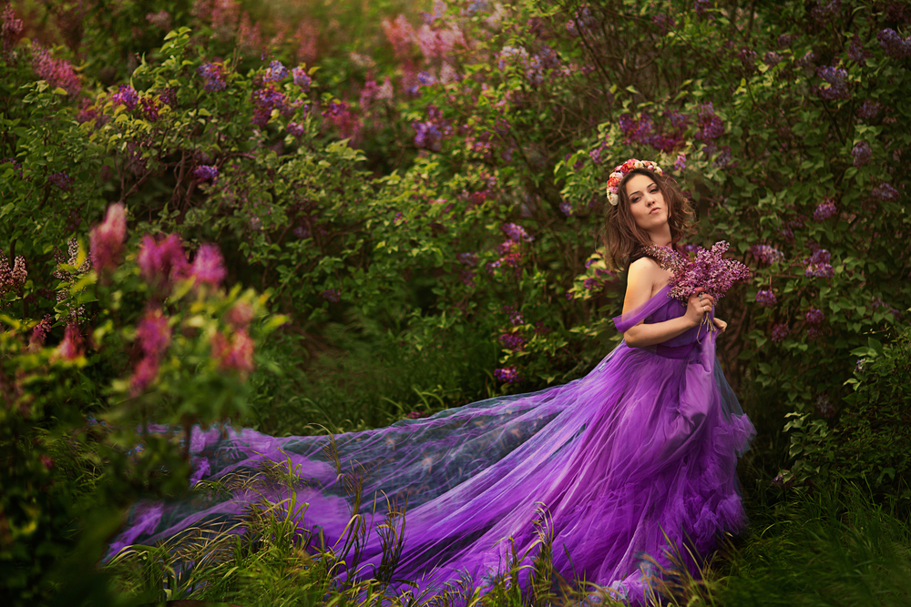 Fată frumoasă îmbrăcată într-o rochie mov, lungă, stă în pădure