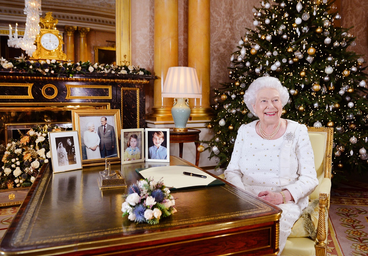 Regina Elisabeta a II-a purtând o rochie albă în timp ce se află la biroul său de la CAstelul Windsor alături de bradul de Crăciun și câteva fotografii ale Familiei Regale Britanice