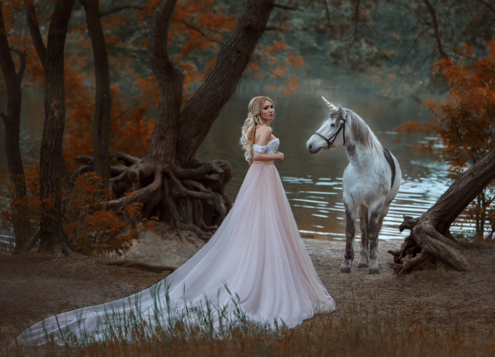 Fată frumoasă îmbrăcată într-o rochie lungă stă în pădure cu un cal