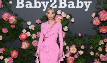 Kim Kardashian poartă o rochie roz, tip sirenă, în cadrul unui eveniment public. Fundalul imaginii este plin de flori roz