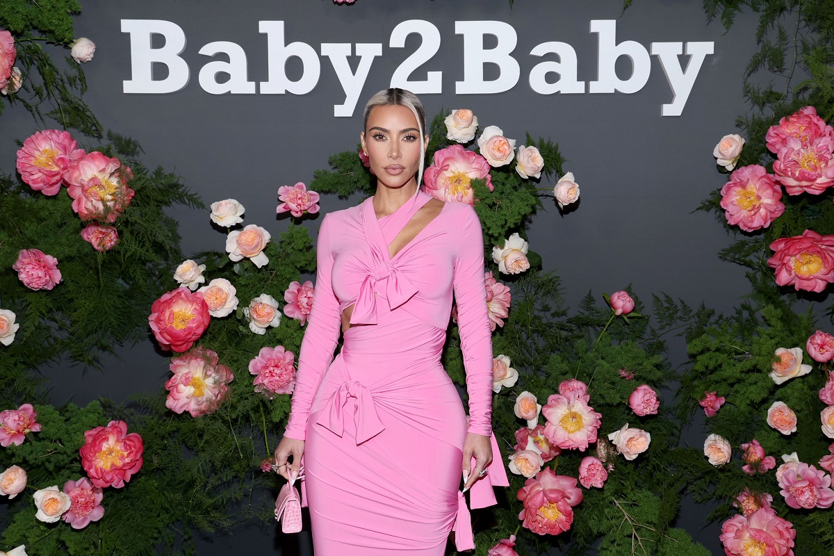 Kim Kardashian poartă o rochie roz, tip sirenă, în cadrul unui eveniment public. Fundalul imaginii este plin de flori roz