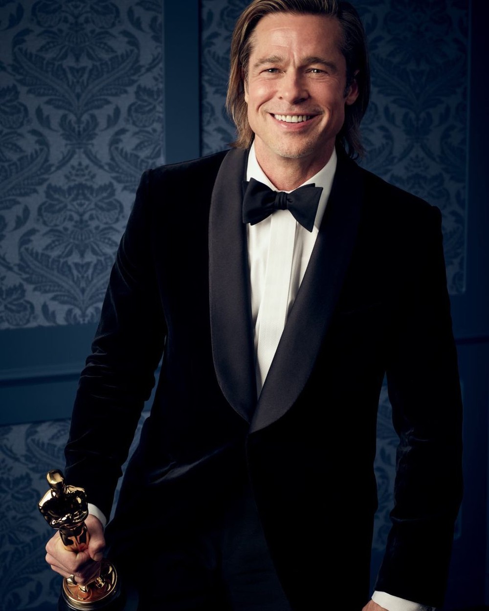 Brad Pitt, într-un costum elegant, cu papion, cu un Oscar în mână