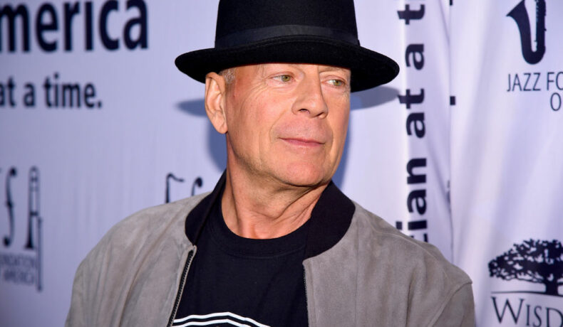 Bruce Willis, cu o pălărie neagră pe cap, la un eveniment, îmbrăcat casual