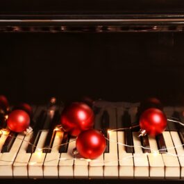 Un pian pe care se află mai multe globuri roșii pentru a ilustra cele mai frumoase piese de Crăciun în 2022