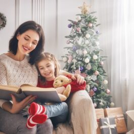 O mămică veselă care îi citește fiicei sale dintr-una din cele mai frumoase cărți de Crăciun pentru copii