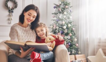 O mămică veselă care îi citește fiicei sale dintr-una din cele mai frumoase cărți de Crăciun pentru copii