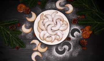 Cornulețe cu nucă și vanilie pe un platou rotund, alături de crengi de brad, conuri, batoane de scorțișoară și anason stelat