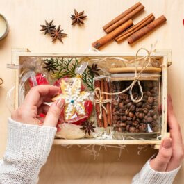 Un coș de lemn cu mai multe cadouri de Crăciun, boabe de cafea, turtă dulce și bețișoare de scorțișoară