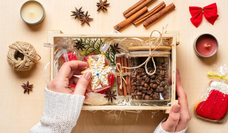 Un coș de lemn cu mai multe cadouri de Crăciun, boabe de cafea, turtă dulce și bețișoare de scorțișoară