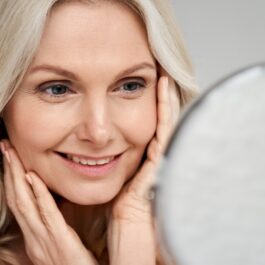 O femeie care se privește în oglindă și aplică câteva sfaturi pentru îngrijirea pielii la menopauză