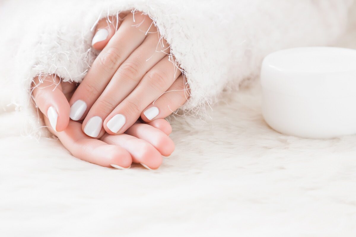 O femeie cu mâini frumoase care își îngrijește unghiile cu cremă în sezonul rece