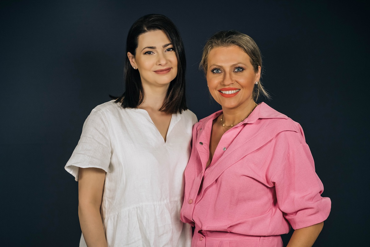 Mihaela Călin într-o rochie albă și Mirela Vaida într-o rochie roz în timp ce pozează împreună pentru seria DePărinți.ro
