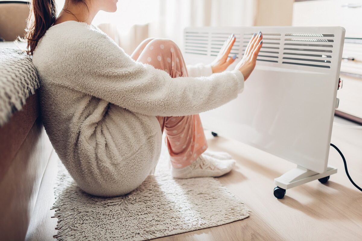 O femeie îmbrăcată gros în pijamale care încearcă să-și încălzească mâinile și picioarele