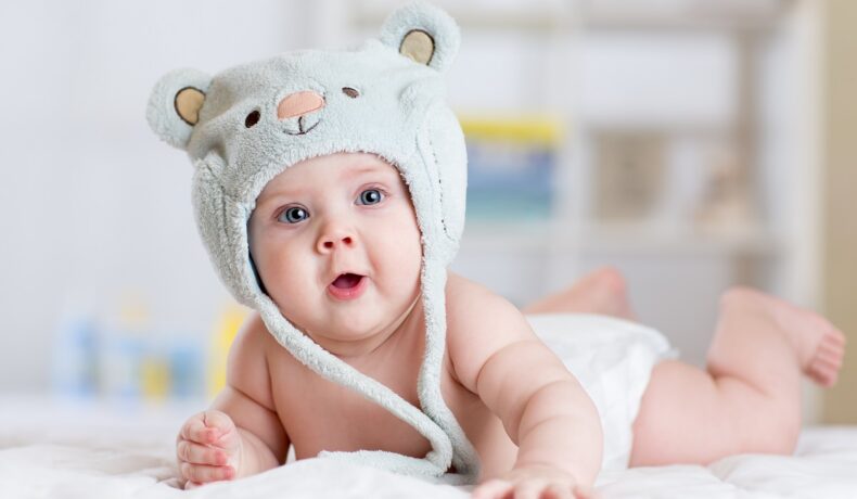 Un bebeluș mic care poartă o căciuliță de ursuleț și zâmbește la cameră