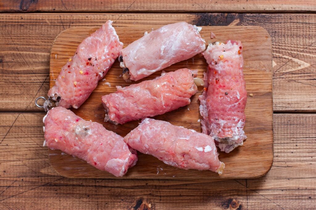 Șase rulouri din carne de porc pe un tocător de lemn