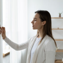 O femeie care face setarea termostatului din casă / Shutterstock
