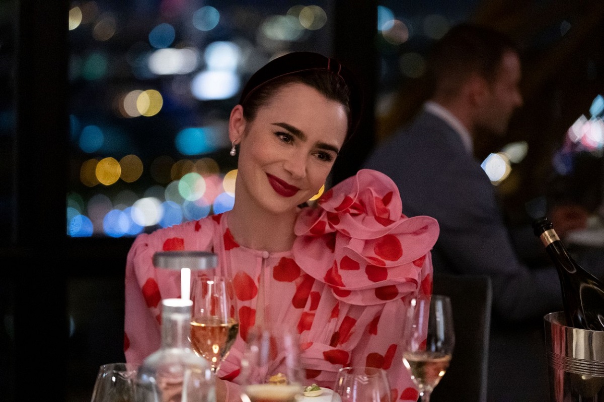 Lily Collins într-o scenă din serialul Emily in Paris în timp ce poartă o rochie roz cu buline roșii