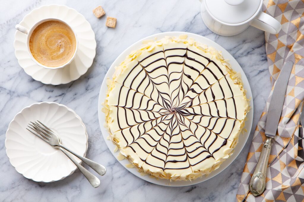 Tort Esterhazy pe un platou alb, alături de o ceașcă de cafea și o farfuriuță cu lingurițe