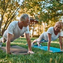 Un cuplu de seniori practică sport într-un parc pe niște saltele de yoga de culori diferite