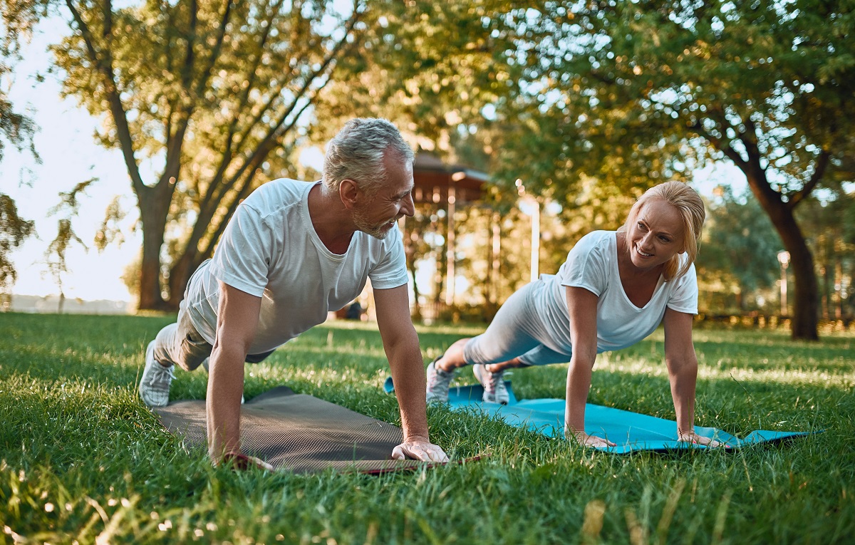 Un cuplu de seniori practică sport într-un parc pe niște saltele de yoga de culori diferite
