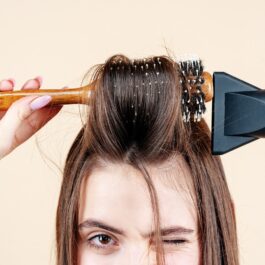 O femeie cu părul deschis la culoare folosește un fohn pentru a-și aranja părul