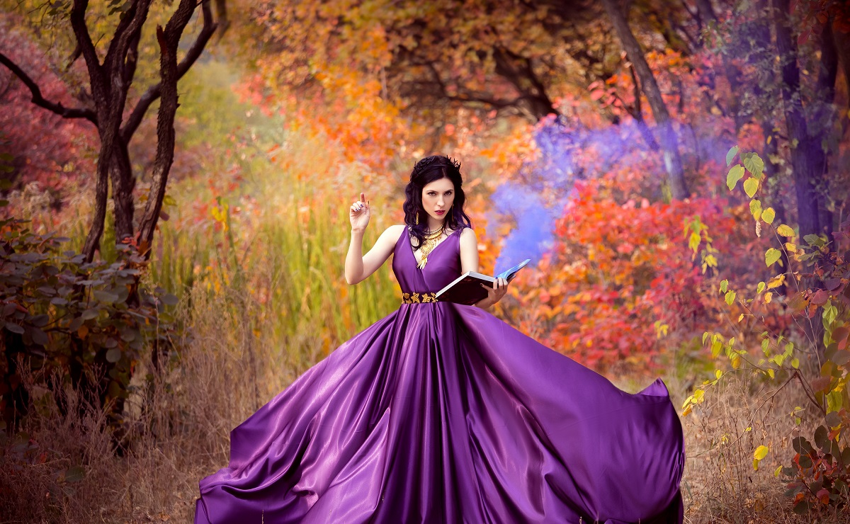 O femeie frumoasă care poartă o rochie violet și pozează într-o pădure ținând o carte în mână pentru a ilustra una dintre zodiile care stăpânesc arta manipulării