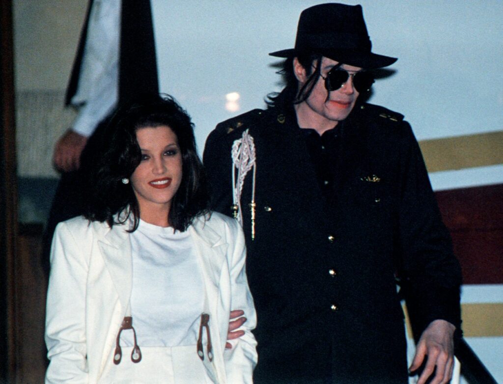 Lisa Marie Presley alături de fostul ei soț, Michael Jackson în cadrul unui eveniment monden, în timp ce poartă un sacou alb, iar Michael haine și ochelari de soare de culoare neagră