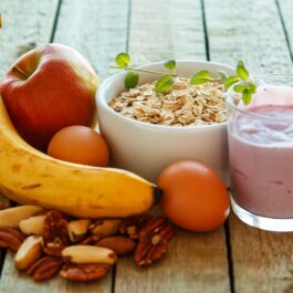 Mai multe alimente care te ajută să ai o zi productivă așezate pe o masă de lemn, printre care o banană, un smoothie, terci de ovăz și alune