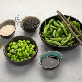 Două bolui cu edamame, noabe verzi de soia imature, alături de sosuri și tacâmuri, unul dintre alimentele cu un conținut mare de acid hialuronic